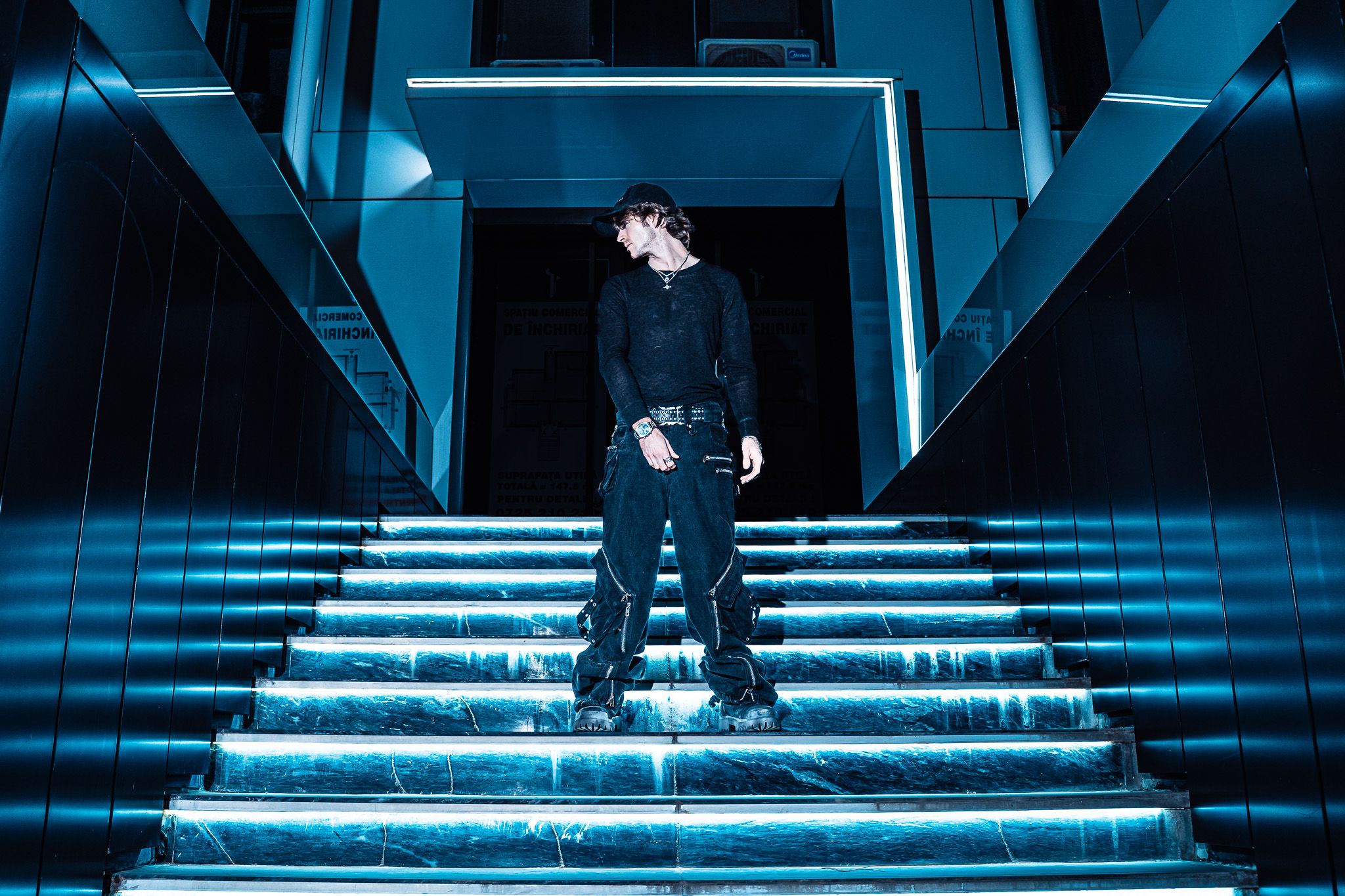 Red Dot standing at the top of a cyan-lit marble staircase at night